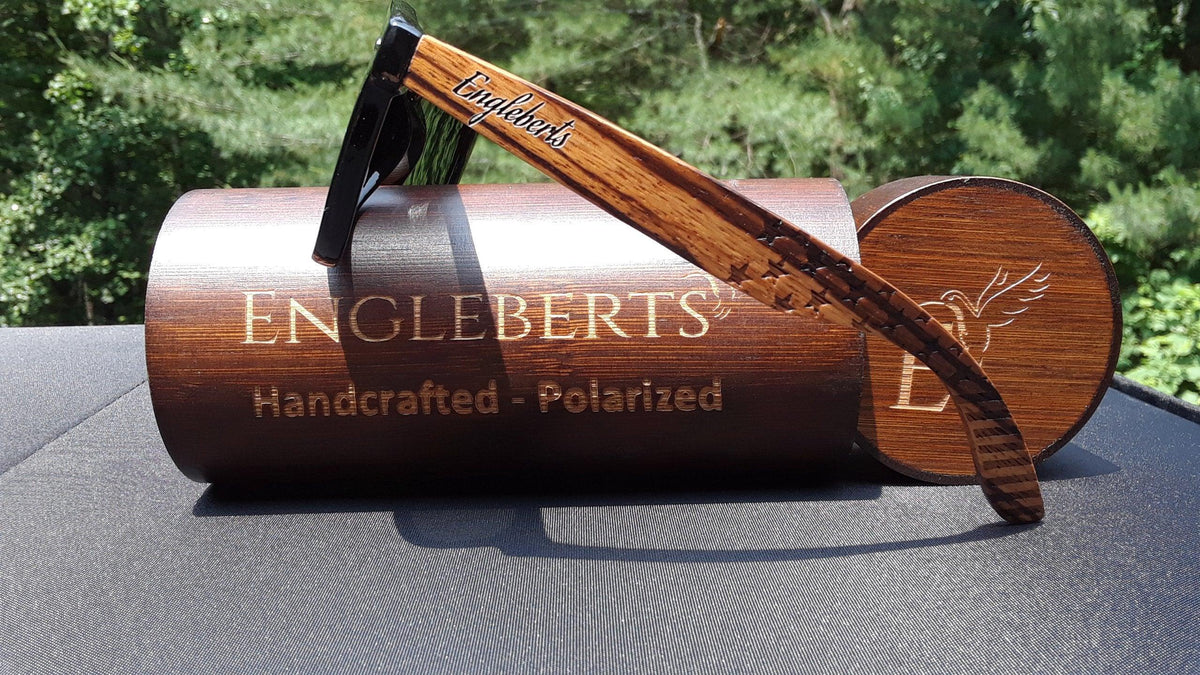Zebrawood sunglasses resting next to bamboo wooden case on a fabric surface