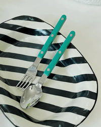 Overhead view of turquoise French rivet cutlery neatly lined up on a white surface.