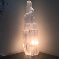 Selenite skyscraper lamp turned on, radiating a warm, calming glow on a clean white background.