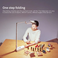 Selfie phone holder extended with ring light on, standing on a wooden table.