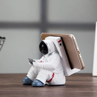 Astronaut desktop phone holder positioned on a light wooden table with natural light.