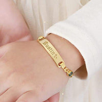 Close-up of personalized toddler bracelet featuring name engraving and small birthstone on silver band.