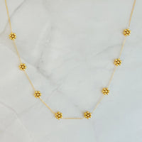 Close-up of delicate golden necklace with tiny bead flowers on a soft white background.