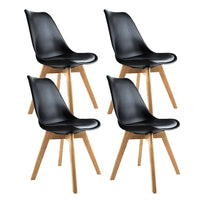 Set of four black padded dining chairs with wooden legs arranged around a white table.