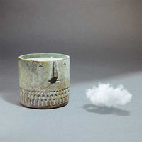 Side view of the unscented stone face candle in a cement vessel showing smooth finish and size scale.