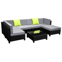 Outdoor 7-piece wicker sofa set with dark cushions and square glass coffee table in backyard setting.