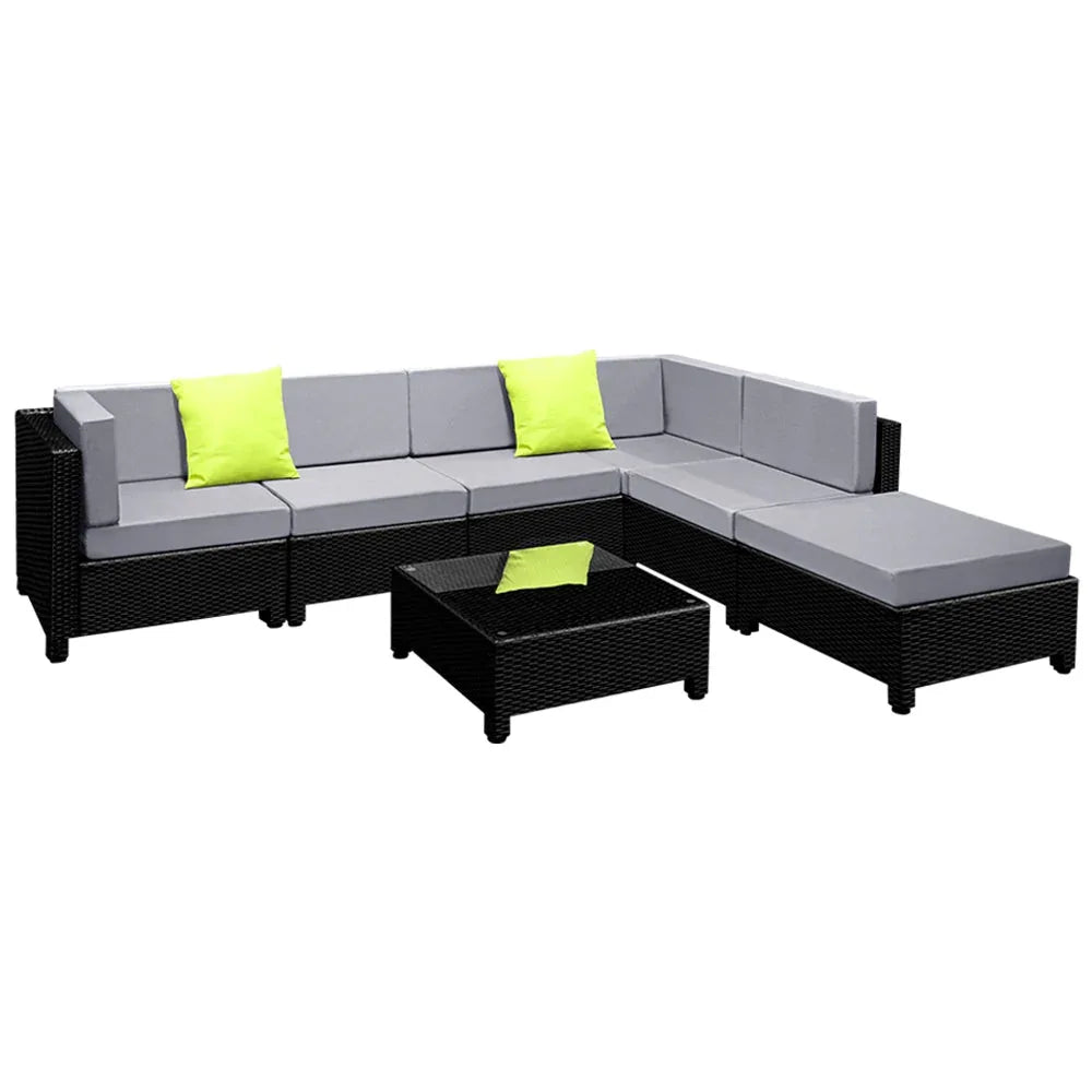 Square outdoor coffee table with tempered glass top beside dark wicker sofa with cushions.