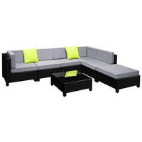 Square outdoor coffee table with tempered glass top beside dark wicker sofa with cushions.