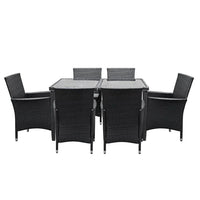 Glass-top outdoor dining table with aluminum frame, surrounded by cushioned rattan chairs