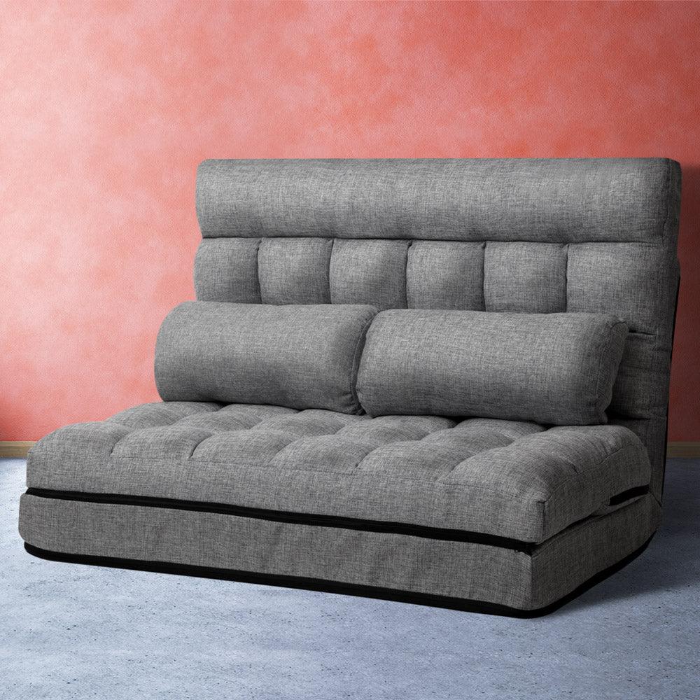 Workspace with laptop and coffee cup beside folded grey Artiss lounge sofa bed on floor.