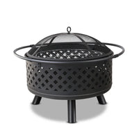 Diamond pattern metal fire pit with glowing fire inside on a patio at night.
