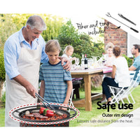 Stainless steel grill plate set on fire pit with glowing embers below.