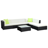 Side view of outdoor wicker sofa set in garden setting with lush green background.