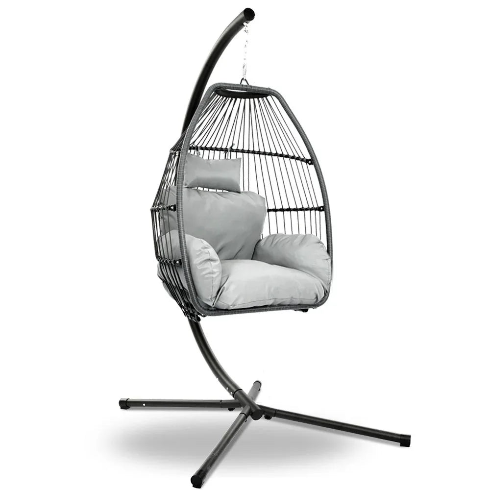 Grey hand-woven wicker hanging egg chair with rope suspension and padded cushion, shown outdoors.