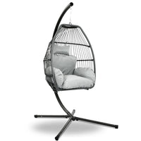Grey hand-woven wicker hanging egg chair with rope suspension and padded cushion, shown outdoors.