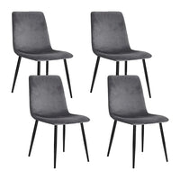 Four modern grey velvet dining chairs with iron legs arranged around a wooden dining table in bright room.