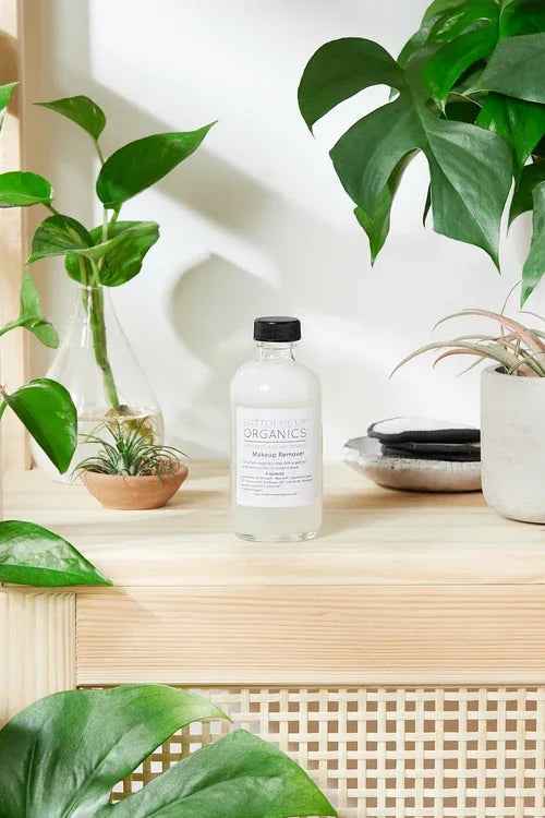Organic makeup remover bottle beside cotton pads on neutral fabric background.