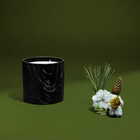 Close-up of black ceramic candle holder with white and gold marquina design, featuring evergreen pine cones.