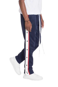 Front view of navy snap button track pants with snap closures down the sides worn by a model.