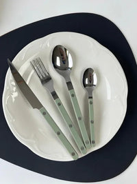 Flatware set with smooth ivory handles including forks, knives, and spoons, styled with greenery on a wooden background.