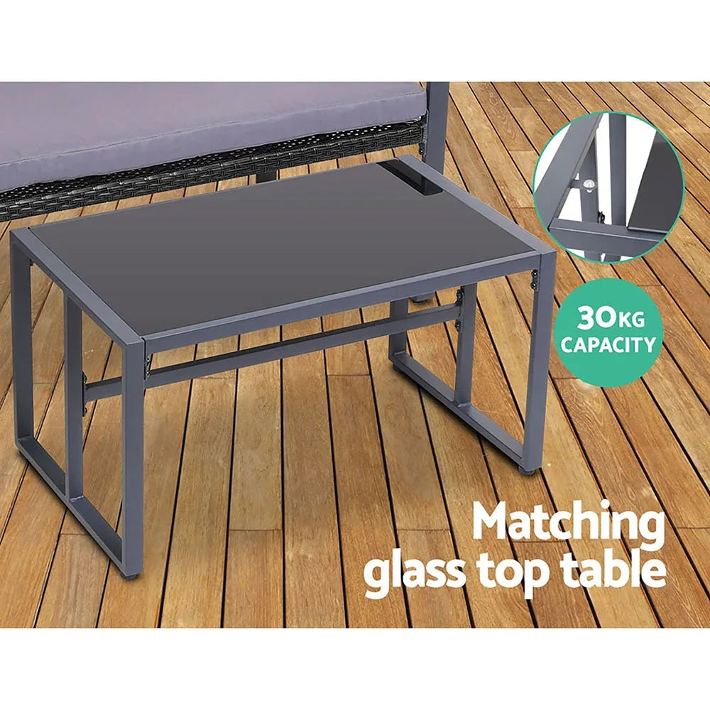 Four black chairs with thick cushions arranged around tempered glass outdoor table.