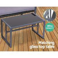 Four black chairs with thick cushions arranged around tempered glass outdoor table.