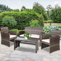 Rattan outdoor furniture set arranged on wooden deck with cushions and glass table, styled for patio.