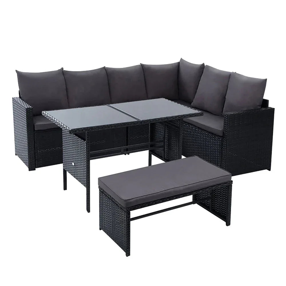 Black wicker outdoor corner sofa with cream cushions under a wooden pergola in garden setting.