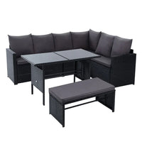 Black wicker outdoor corner sofa with cream cushions under a wooden pergola in garden setting.