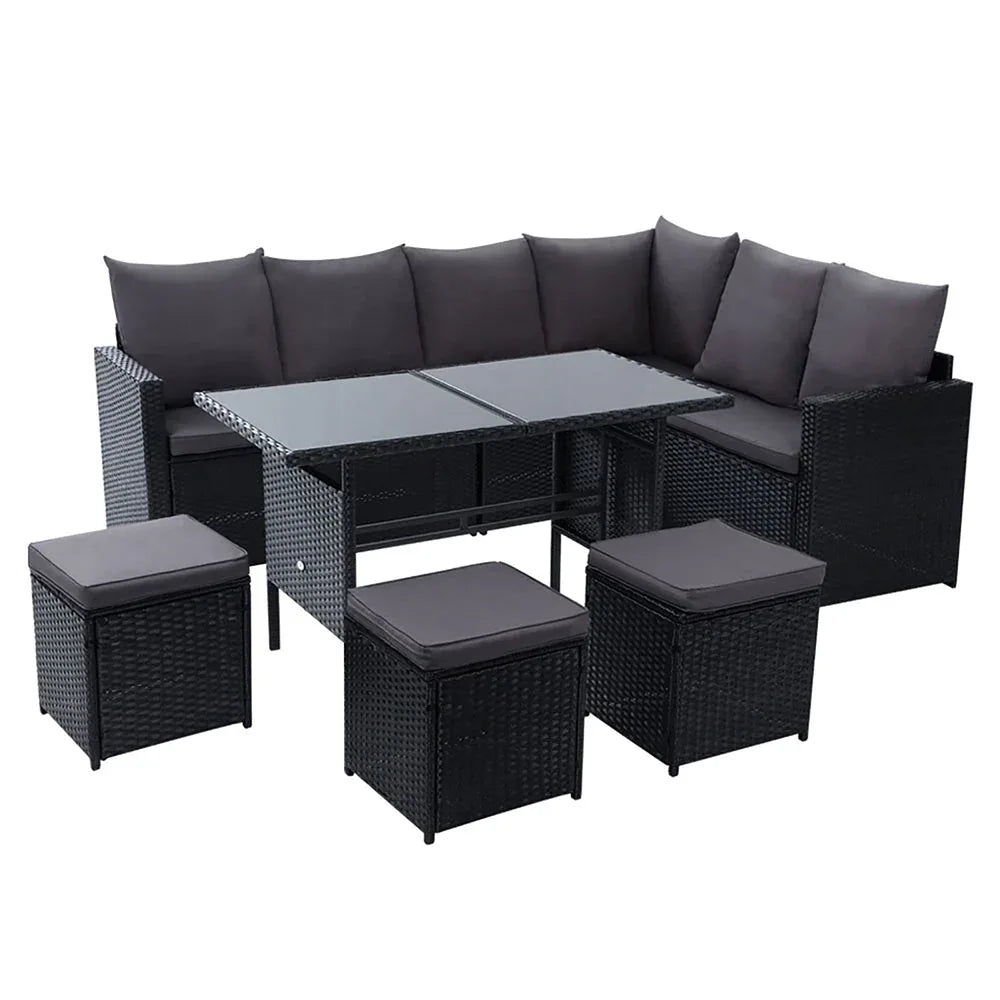 Outdoor dining sofa set with black wicker and beige cushions arranged on patio beside green plants.