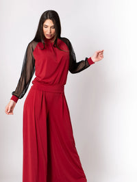 Woman wearing garnet palazzo pants and silk knit top with long sheer tulip sleeves, standing against white background.