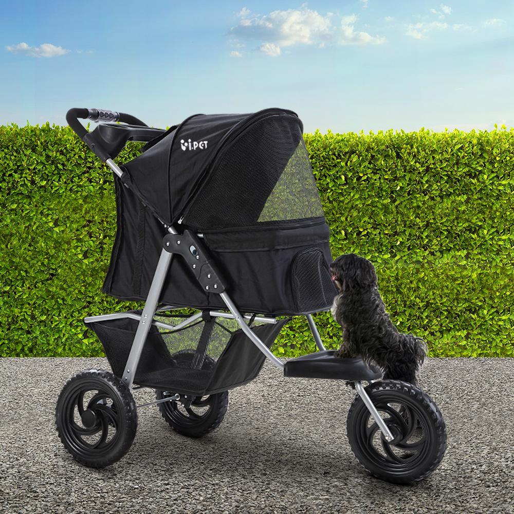 Black i.Pet pet stroller next to a small dog outdoors on pavement