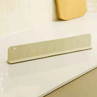Gray silicone sink splash guard with suction cups attached, placed along a kitchen sink edge to prevent water splashing.