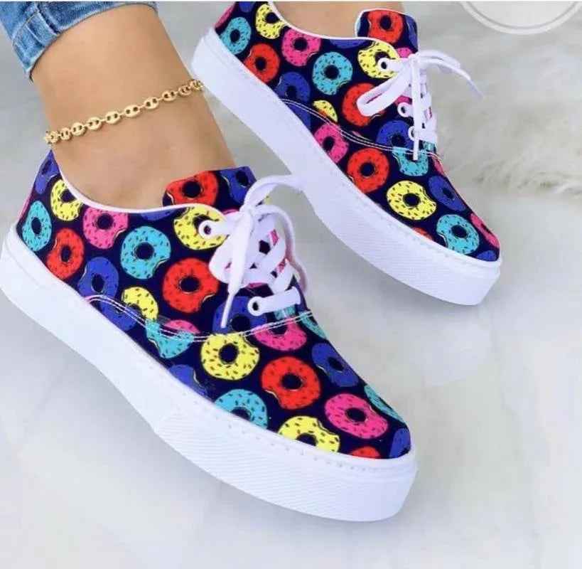 White women’s sneakers with colorful graffiti-style designs, lace-up closure, and a chunky sole on a neutral background.