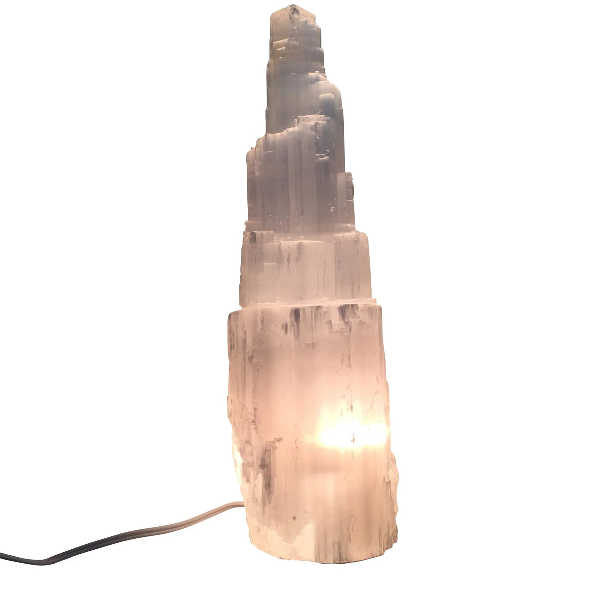 Tall selenite crystal lamp shaped like a skyscraper emitting soft white light on a white surface.