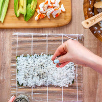 Sushi making kit with bamboo rolling mats and utensils arranged for easy sushi rolling.