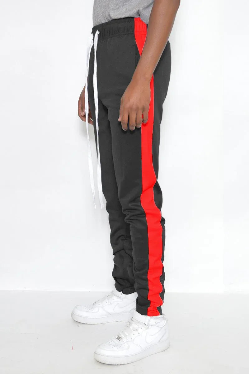 Side angle of men's slim fit black track pants highlighting red stripe and ankle zipper details.