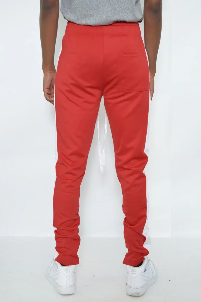 Side profile of red men's track pants with white stripe and ankle zipper visible.