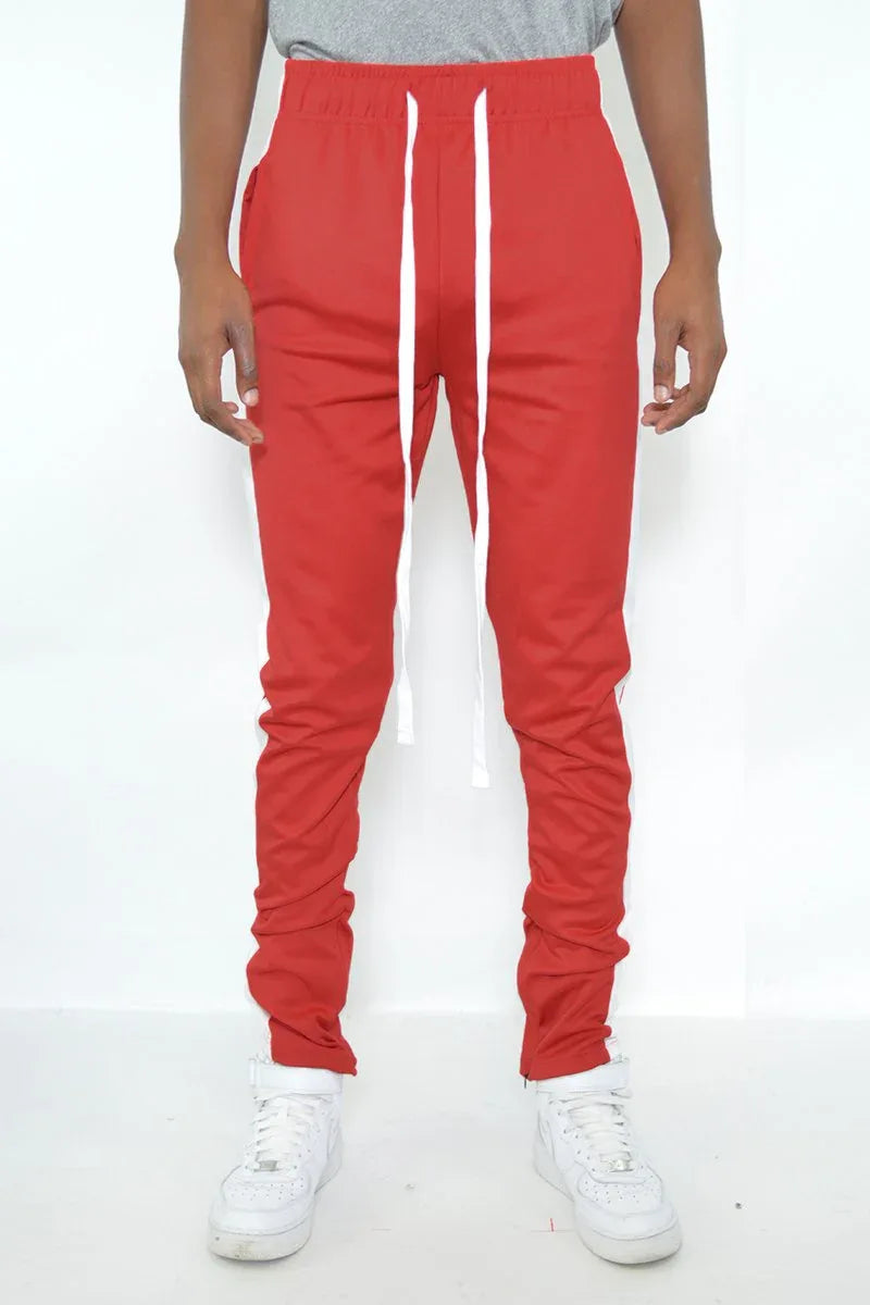 Close-up of red track pants showing zipper and white stripe detail on side.
