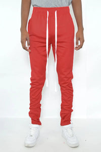 Close-up of red track pants showing zipper and white stripe detail on side.
