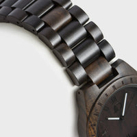 Men's wood watch displayed with textured black walnut face and silver details on wrist.