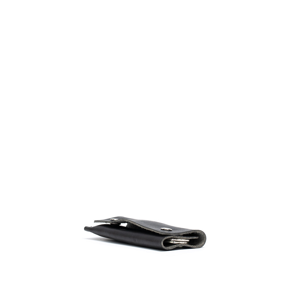 Close-up of leather key case with AirTag inserted, showing metal key rings and strap.