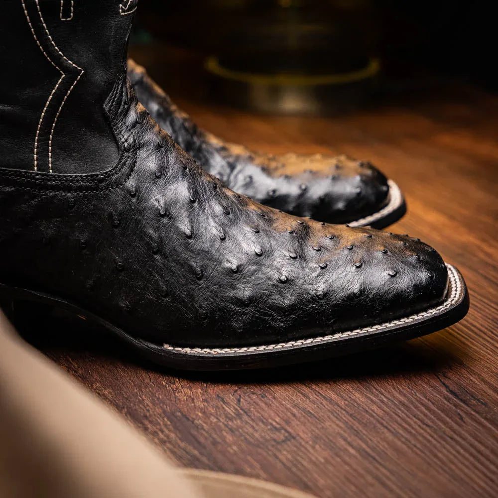 Side view of black ostrich skin cowboy boots worn with jeans in casual outdoor setting.