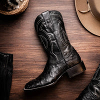 Close-up of black ostrich skin cowboy boots on feet, showing texture and design details.