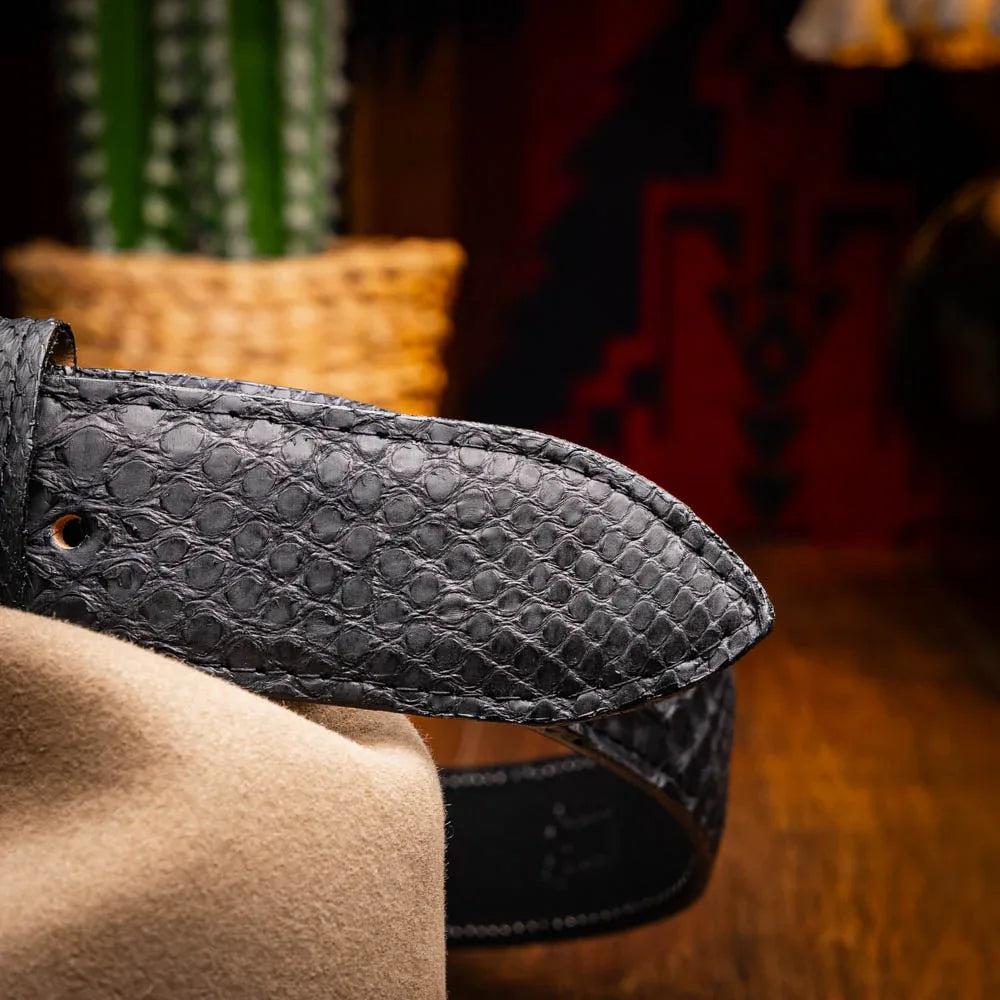 Person seated wearing Arkansas black python belt paired with dark denim and leather boots