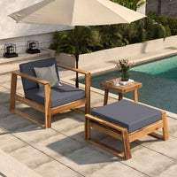 Acacia wood outdoor lounge chair with grey cushions and matching ottoman on stone patio.