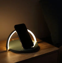 A sleek black wireless charging block holds a smartphone upright on a wooden desk, charging the device.