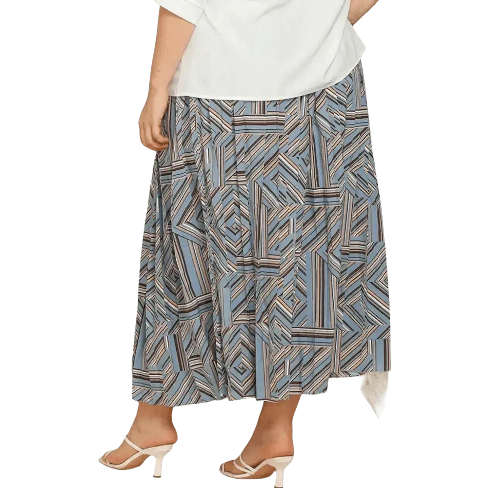 Model wearing blue geometric pleated skirt in deep teal, styled with a white top and black shoes.