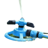 Blue automatic rotating garden sprinkler spraying water over green grass on sunny day.