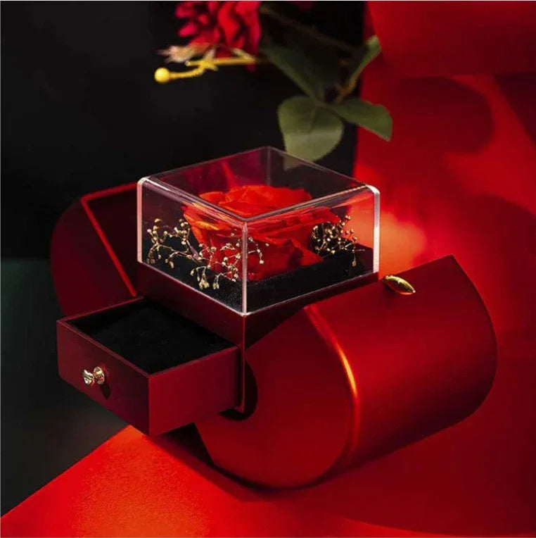 Open red apple jewelry box showing preserved rose and small drawer for jewelry storage.